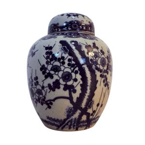 Puede incluir: Un tarro de jengibre de cerámica blanca y azul con tapa. El tarro está decorado con un estampado floral en azul oscuro. El diseño presenta ramas y flores florecientes. El tarro tiene forma redondeada.