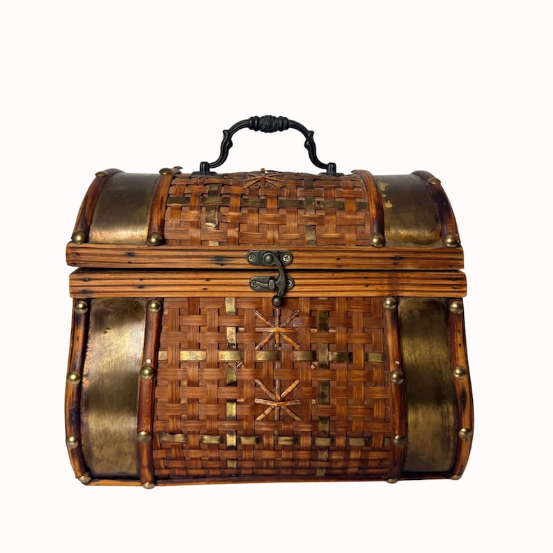 May include: A decorative chest with a woven bamboo body, accented with brass-colored metal trim and studs. It features a black handle and a latch closure. The chest has a vintage, rustic aesthetic.