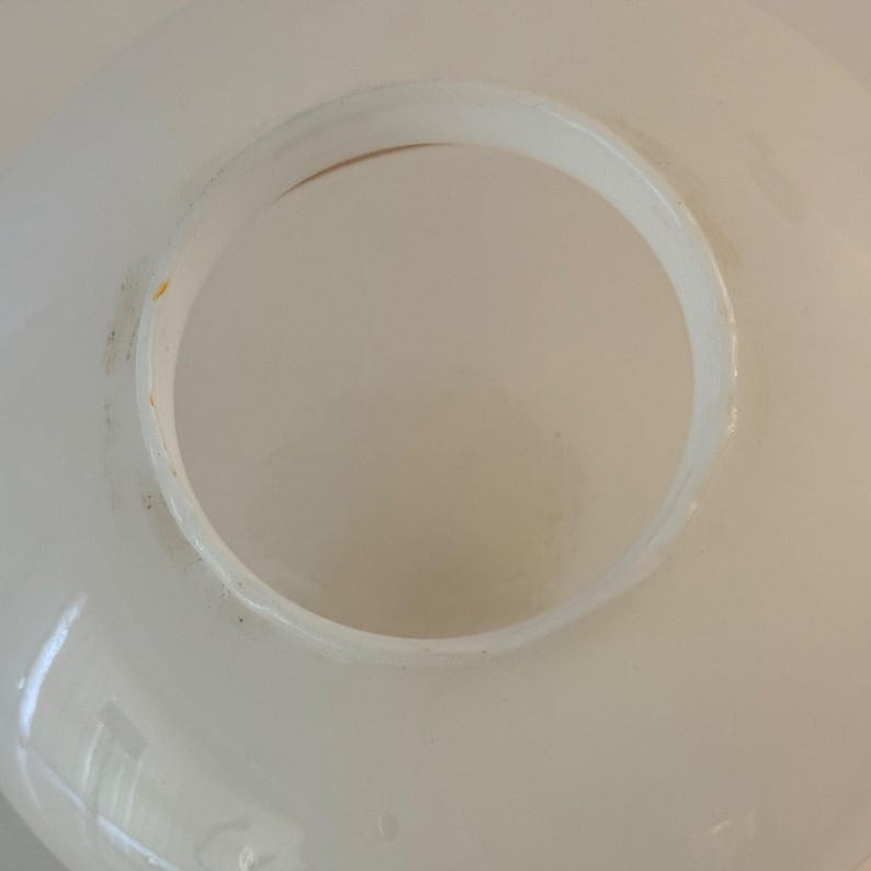 May include: A close-up view of a white, circular object with a large, central opening. The object has a smooth, glossy surface with a slightly uneven edge around the opening. The interior of the opening is a light beige color.
