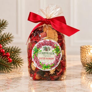 May include: A clear plastic bag filled with red and tan potpourri, tied with a red satin ribbon. A circular label features a wreath graphic and the text: COUNTRYSIDE FRAGRANCES WINTER BAYBERRY NET WT. 4 OZ. / 113 G. The bag contains dried botanical elements.
