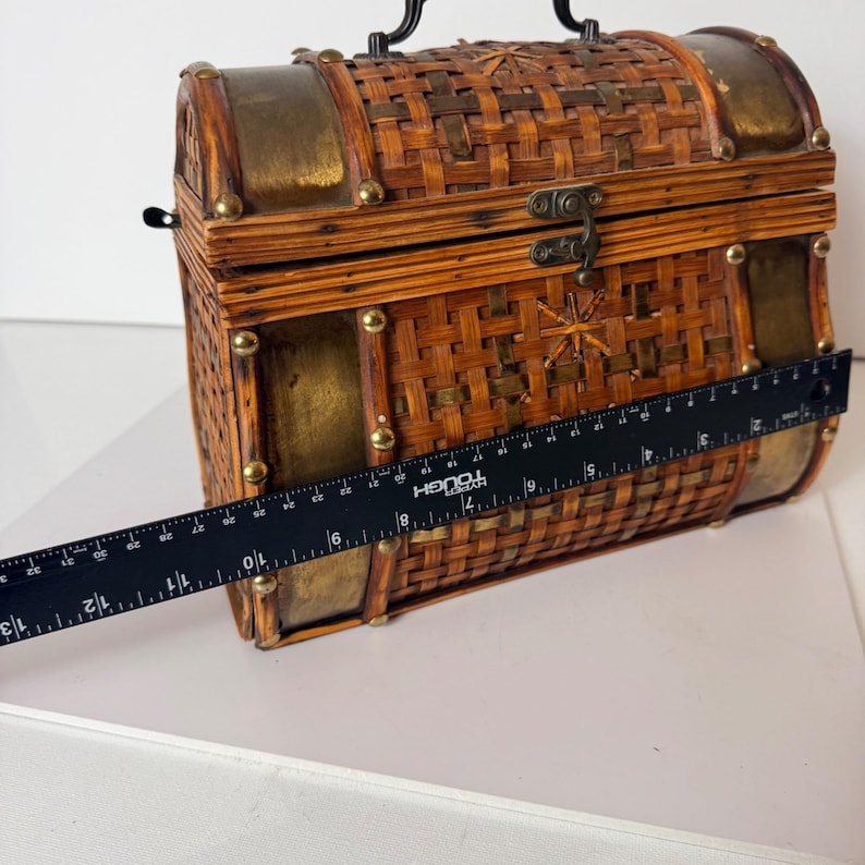 May include: A decorative, woven chest with brass accents and a black handle. The chest is approximately 13 inches long. The chest has a starburst design on the front and is secured with a metal clasp. The chest is made of woven wood.