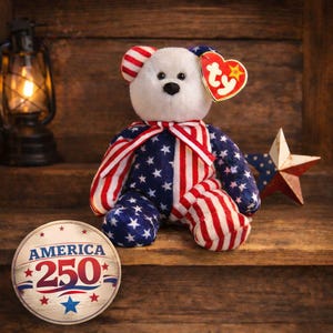 May include: A patriotic plush bear with a white head, red and white striped ears and paws, and a body adorned with a blue star-studded pattern and red and white stripes. A red heart-shaped tag is attached. A wooden star and a commemorative coin are also present.
