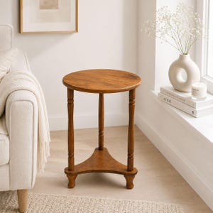 May include: A round, wooden side table with a warm brown finish. The table has a three-legged base and a triangular shelf. The table is approximately 24 inches tall and 18 inches in diameter, perfect for a living room or bedroom.