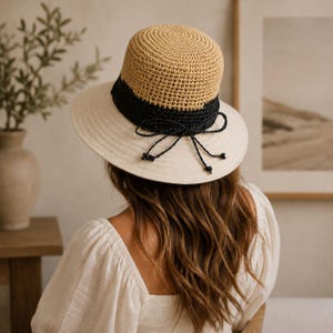 Può includere: Cappello da sole beige e nero con tesa larga. Il cappello presenta una corona rotonda intrecciata di colore beige chiaro, una fascia nera e un fiocco abbinato. La tesa è di colore beige chiaro. Questo cappello è ideale per la protezione solare.