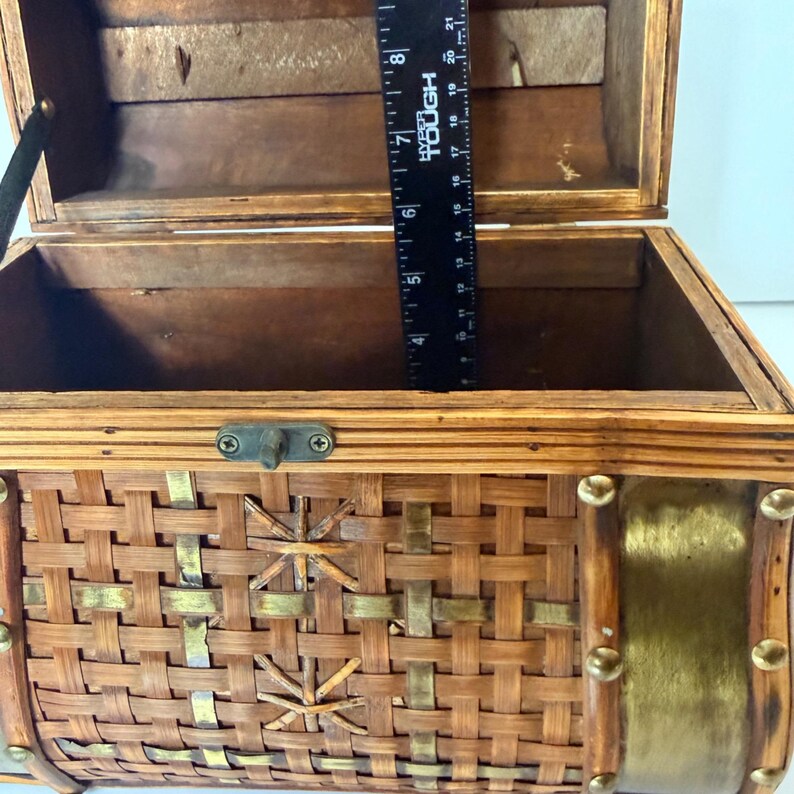 May include: Open wooden chest with a woven bamboo exterior and brass accents. The chest has a hinged lid and a metal clasp closure. A ruler is inside the chest, measuring approximately 8 inches in height.