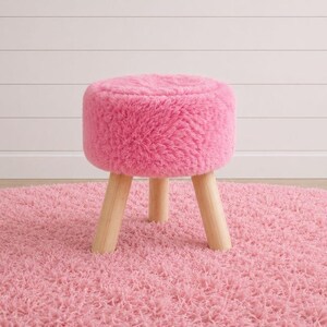 May include: A round stool featuring a thick, plush, bright pink faux fur seat cushion. The stool is supported by three sturdy, light-colored wooden legs that are cylindrical in shape and provide a stable base for the soft, textured top surface.