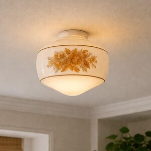 May include: A vintage-style ceiling light fixture with a white, rounded glass shade. The shade features a floral pattern in shades of yellow and brown, with a thin brown band. The fixture is mounted on a white ceiling.