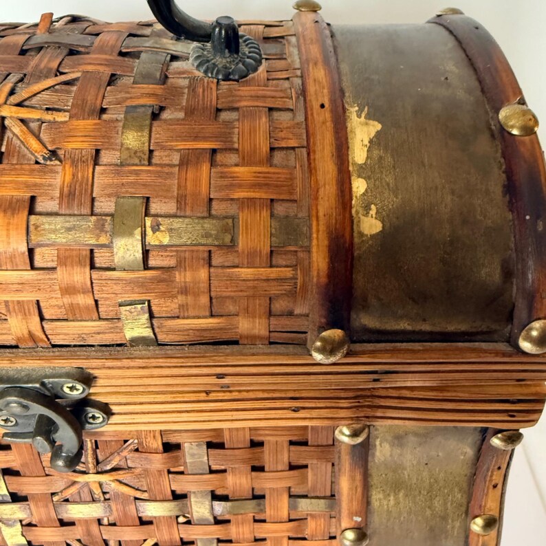 May include: A decorative chest with a woven bamboo design. The chest features brass accents, a black handle, and a metal clasp. The edges are trimmed with dark wood and brass studs. The chest is a warm brown color.