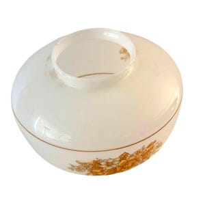 May include: A vintage, off-white glass lampshade with a rounded shape and a wide opening. The shade features a decorative band of yellow and brown floral patterns around the base. A thin brown line accents the design.