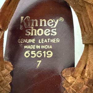May include: Close-up of the insole of a brown leather shoe. The insole is stamped with "Kinney Shoes", "Genuine Leather", "Made in India", and the number "65619". The shoe size is 7.