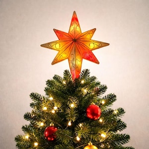 Könnte beinhalten: Ein mehrzackiger Stern als Baumspitze mit einem Farbverlauf in Orange- und Gelbtönen sowie dunklen, geschwungenen Filigranmustern. Der Stern sitzt auf einem grünen künstlichen Weihnachtsbaum, der mit warmweißen Lichterketten und roten Kugeln geschmückt ist.