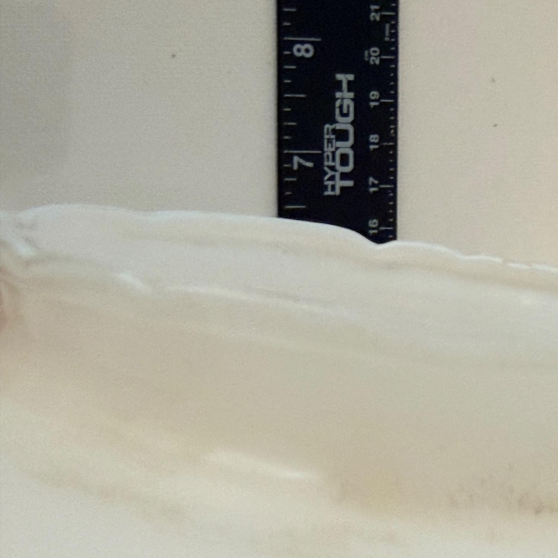 May include: A black ruler with white markings and the text "HYPER TOUGH" is positioned vertically against a white, textured surface. The ruler measures up to 8 inches.