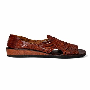May include: Brown leather sandal with a woven design. The sandal features a low wooden heel and a dark brown sole. The upper part of the sandal is made of interwoven leather strips, creating an open, airy design. The sandal is designed for comfort and style.