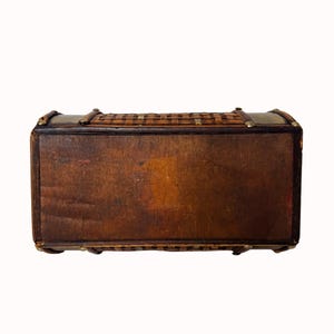 May include: A vintage wooden chest with a woven top and brass accents. The chest is rectangular with a dark brown finish and a woven, basket-like top. The corners and edges are reinforced with brass hardware. The chest is likely used for storage.