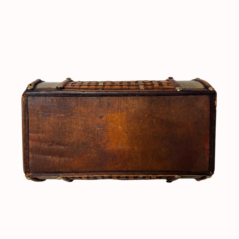 May include: A vintage wooden chest with a woven top and brass accents. The chest is rectangular with a dark brown finish and a woven, basket-like top. The corners and edges are reinforced with brass hardware. The chest is likely used for storage.