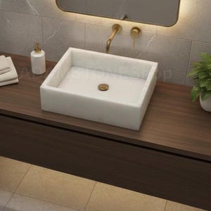 Könnte beinhalten: Ein modernes Badezimmer-Waschbecken mit einem rechteckigen weißen Waschbecken, einer goldenen Armatur und einem Spiegel mit goldenem Rahmen. Der Waschtisch aus dunklem Holz hat eine kleine Pflanze und einen Seifenspender. Die Wände sind hellgrau gefliest. Das Waschbecken ist ca. 40 cm breit.