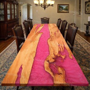 Könnte beinhalten: Ein großer, rechteckiger Esstisch mit einem leuchtend rosa Harzmittelstück und natürlichen Holzkanten. Der Tisch ist von dunkelbraunen Lederstühlen umgeben, was einen auffälligen Kontrast erzeugt. Der Tisch ist etwa 244 cm lang und 102 cm breit.