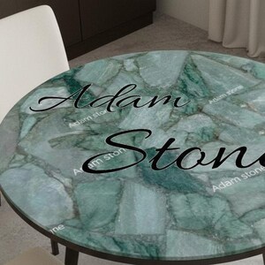 May include: A round table with a green stone top and dark legs. The tabletop features a mosaic pattern with shades of green and gray. The text "Adam Stone" is written across the top. Two white chairs are visible.
