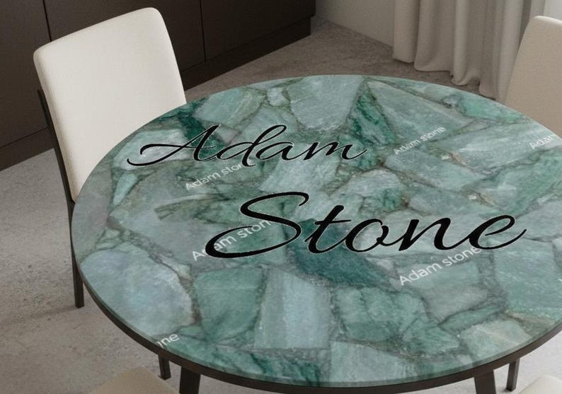 May include: A round table with a green stone top and dark legs. The tabletop features a mosaic pattern with shades of green and gray. The text "Adam Stone" is written across the top. Two white chairs are visible.