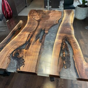 Könnte beinhalten: Ein großer Esstisch aus Walnussholz mit einer natürlichen Kante und einer Einlage aus klarem Epoxidharz. Der Tisch hat ein natürliches, rustikales Aussehen und passt perfekt zu einem modernen oder Landhausstil.