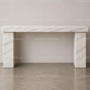 Puede incluir: Una consola rectangular de mármol con un patrón veteado blanco y gris. La mesa tiene una parte superior gruesa y dos patas rectangulares. El texto "ADAMSTONEShop" se repite en la imagen.