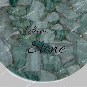 May include: Circular stone surface with a mosaic pattern in shades of green and gray. The text "Adam Stone" is displayed in a cursive font across the center of the stone.