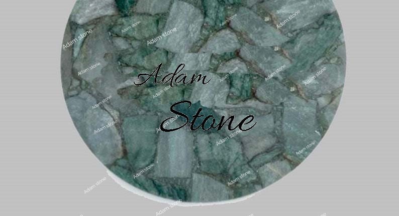 May include: Circular stone surface with a mosaic pattern in shades of green and gray. The text "Adam Stone" is displayed in a cursive font across the center of the stone.