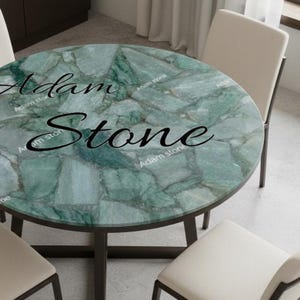 May include: A round dining table with a green stone top and a dark metal base. The table is surrounded by four cream-colored chairs. The text "Adam Stone" is printed on the table's surface.