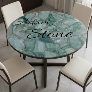 May include: A round dining table with a green stone top and dark brown legs. The table is surrounded by four white chairs with dark brown frames. The text "Adam Stone" is printed on the table's surface.