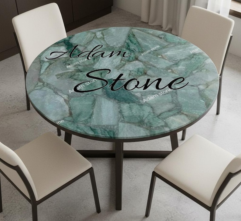 May include: A round dining table with a green stone top and dark brown legs. The table is surrounded by four white chairs with dark brown frames. The text "Adam Stone" is printed on the table's surface.