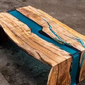 Op de afbeelding: Een houten salontafel met een blauwe harsrivier die door het midden loopt. De tafel heeft een natuurlijke, rustieke uitstraling en is gemaakt van één stuk hout.
