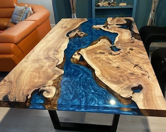 May include: A large wooden dining table with a blue epoxy resin river running through the center. The table has a black metal base.