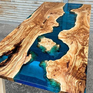 Könnte beinhalten: Eine Tischplatte aus Holz mit einem blauen und grünen Epoxidharzfluss, der durch sie verläuft. Das Holz hat eine natürliche Maserung und das Harz ist glatt und glänzend.