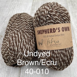 May include: Two skeins of Shepherd's Own 100% all natural undyed wool yarn in a brown and ecru marled colorway. The label features a sheep illustration and the text Shepherd's Own, 100% All Natural Undyed Wool, Fibra Natura, Undyed Brown/Ecru 40-010.