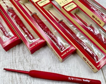 May include: A collection of red Tulip Etimo crochet hooks, each featuring a soft-grip handle and a metal hook tip. Several hooks are enclosed in their original beige and red cardboard packaging, labelled with sizes like 1.80mm, 2.20mm, and 3.00mm.