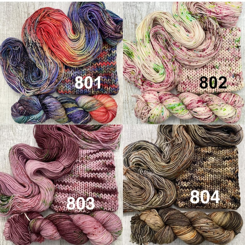 May include: Four sets of hand-dyed yarn skeins and matching knitted swatches labelled 801, 802, 803, and 804. Set 801 features vibrant red, purple, and blue tones. Set 802 is cream with green and pink speckles. Set 803 is dusty pink and mauve. Set 804 is brown and tan.