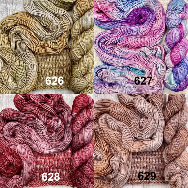 May include: Four skeins of yarn with matching knitted swatches, labelled 626 in tan, 627 in variegated pink and blue, 628 in deep red, and 629 in light brown. Each set displays the yarn texture and colour variation clearly.