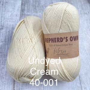 May include: Two skeins of cream-colored yarn. The right skein features a brown paper label with the text Shepherd's Own, 100% All Natural Undyed Wool, and Fibra Natura. The text Undyed Cream 40-001 is overlaid on the lower portion of the image.