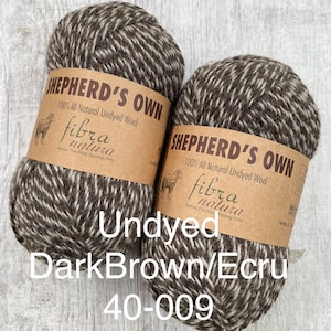 May include: Two skeins of Shepherd's Own 100% all natural undyed wool yarn in a dark brown and ecru marled colorway. Each skein features a tan paper label with the text Shepherd's Own, Fibra Natura, and an illustration of a sheep.