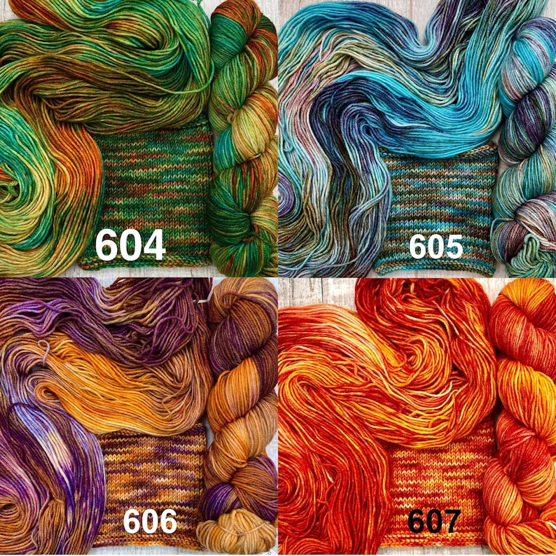 May include: Four skeins of hand-dyed yarn with matching knitted swatches labelled 604, 605, 606, and 607. The yarn colours include green and orange, blue and purple, purple and gold, and vibrant red and orange variegated tones.