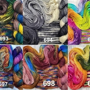 May include: Six sets of hand-dyed yarn skeins and knitted swatches labelled 693 through 699. Each set features distinct colour palettes including earth tones, monochromatic greys, vibrant rainbows, and deep jewel tones in various fibre textures.