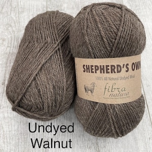 May include: Two skeins of dark brown, undyed wool yarn labeled Shepherd's Own 100% All Natural Undyed Wool by Fibra Natura. The label features a small illustration of a sheep and the text Undyed Walnut 40005 is printed below the yarn.