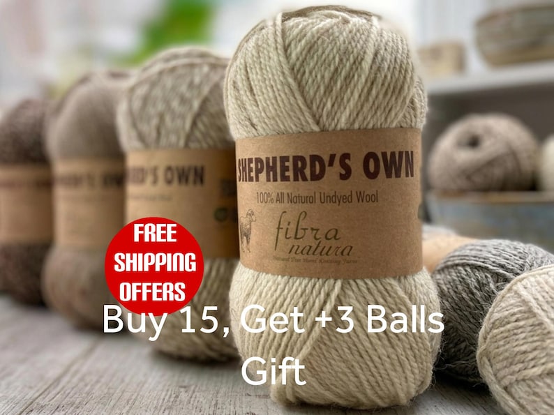 May include: A ball of light beige, undyed wool yarn with a brown paper label reading Shepherd's Own 100% All Natural Undyed Wool and Fibra Natura. The yarn has a thick, twisted texture, and several other balls of yarn in various neutral shades are visible.