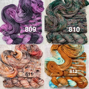 May include: Four skeins of hand-dyed yarn with matching knitted swatches. The yarn colours include purple and black labelled 809, green and brown labelled 810, orange and cream labelled 811, and gold and turquoise labelled 812.