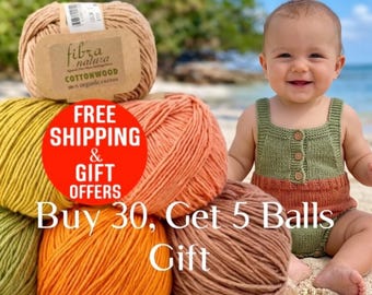 May include: A stack of Fibra Natura Cottonwood yarn balls in shades of tan, yellow, orange, and brown, alongside a knitted olive green romper with three small buttons on the front chest area.