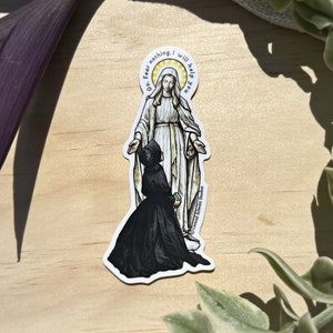 Peut inclure: Un autocollant représentant une image religieuse de la Vierge Marie avec une femme agenouillée devant elle. Le texte autour de la Vierge Marie dit "Go Fear nothing, I will help you".