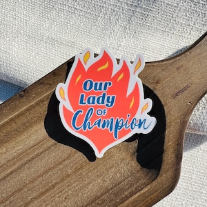 Peut inclure: Un autocollant en forme de flamme rouge et jaune avec le texte "Our Lady of Champion" en lettres bleues et blanches.