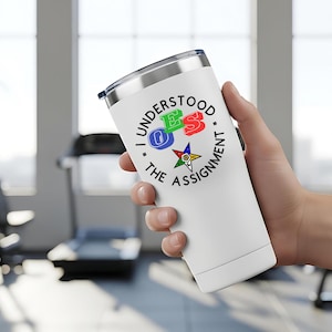 May include: White insulated tumbler with a silver lid, held in a hand. The tumbler features a circular design with the text "I UNDERSTOOD THE ASSIGNMENT" and the letters OES in blue, green, and red, with a star symbol.
