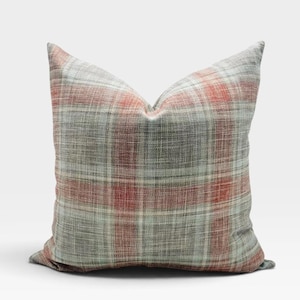 May include: A square throw pillow featuring a woven plaid pattern in shades of muted sage green, soft gray, and warm terracotta orange. The fabric has a visible textured weave, and the pillow is plumped to create a soft, rounded shape.