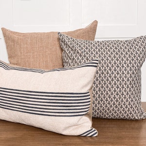 May include: Three decorative throw pillows with different patterns. The pillow on the left has white and black stripes. The middle pillow is a light brown with a woven texture. The pillow on the right has a gray and white floral pattern.